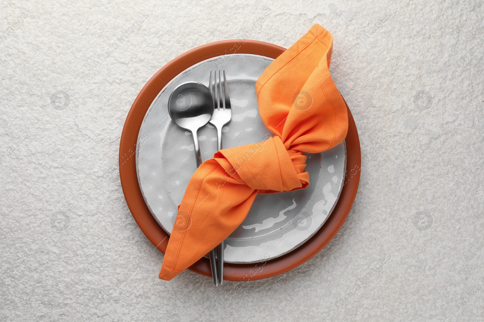 Photo of Stylish setting with cutlery, napkin and plates on light textured table, top view