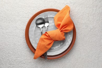 Stylish setting with cutlery, napkin and plates on light textured table, top view