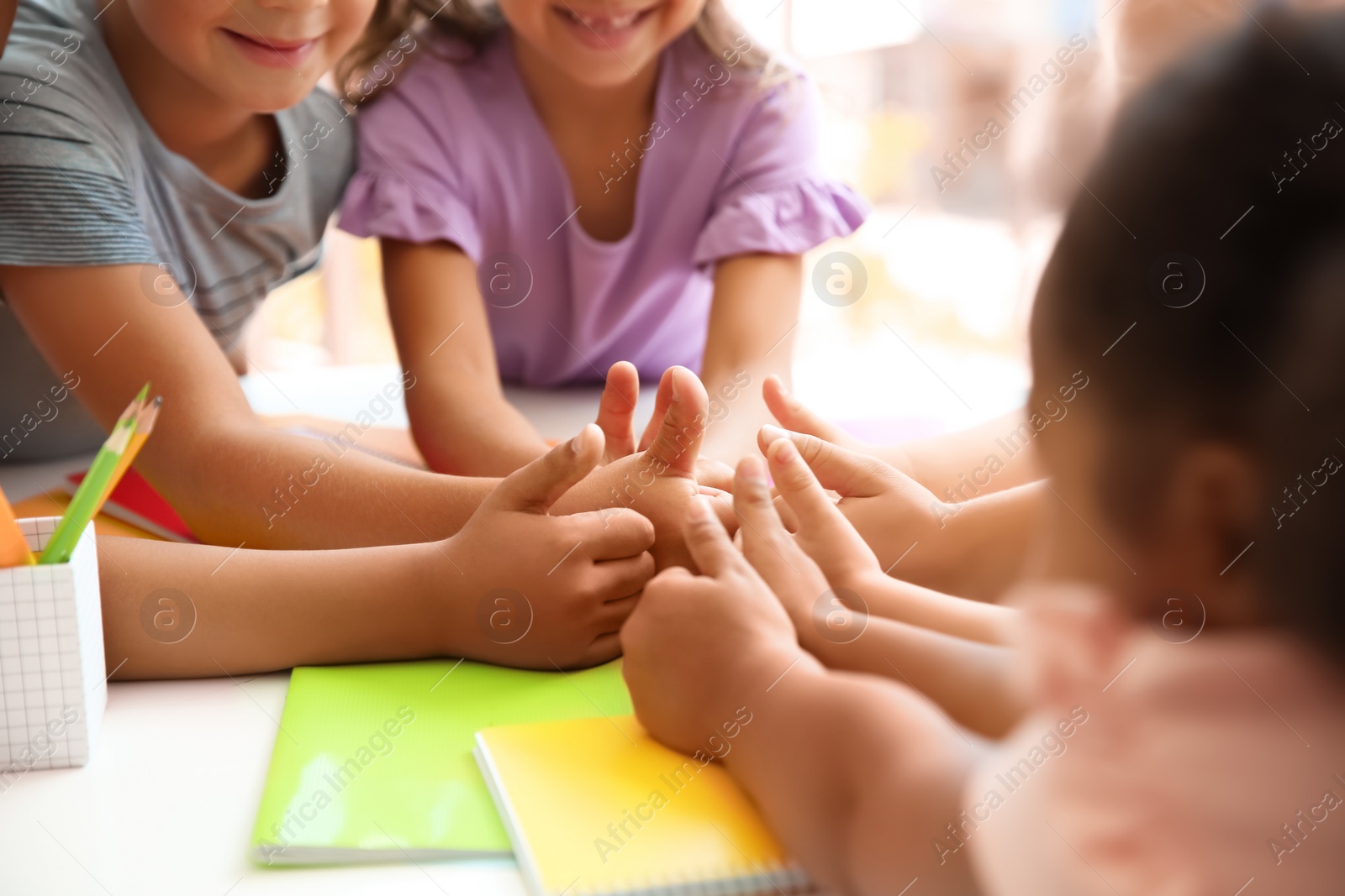 Photo of Little children putting their hands together at table, closeup. Unity concept