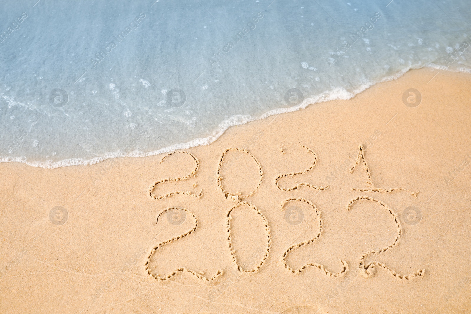 Photo of Dates written on sandy beach. 2021 washed by sea wave as New 2022 Year coming, above view