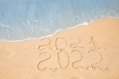 Photo of Dates written on sandy beach. 2021 washed by sea wave as New 2022 Year coming, above view