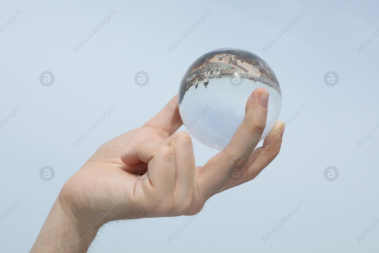 Photo of View of beautiful city street, overturned reflection. Man holding crystal ball against sky, closeup