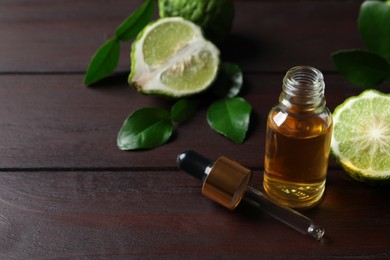 Photo of Bottle of essential oil, pipette and fresh bergamot fruit on wooden table. Space for text