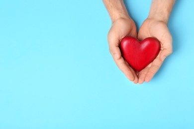 Young man holding red heart on light blue background, top view with space for text. Donation concept