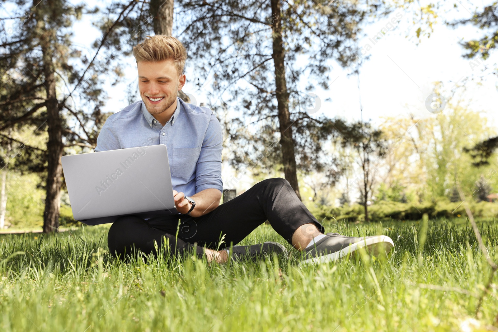 Image of Young man working on laptop in park