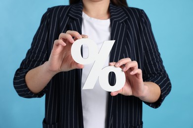 Photo of Woman holding percent sign on light blue background, closeup