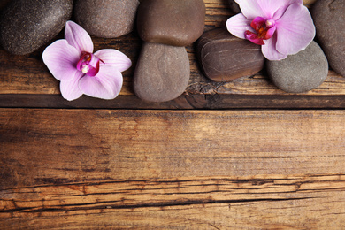 Stones with orchid flowers and space for text on wooden background, flat lay. Zen lifestyle