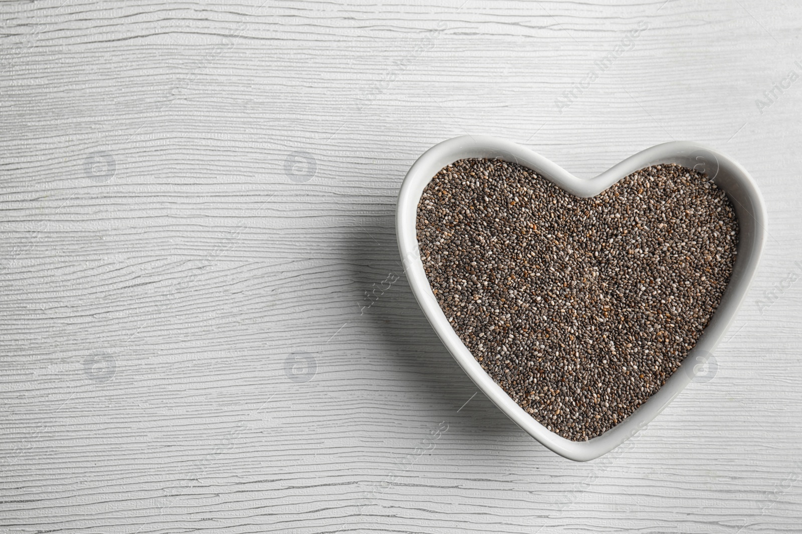 Photo of Heart shaped bowl with chia seeds on wooden background, top view. Space for text