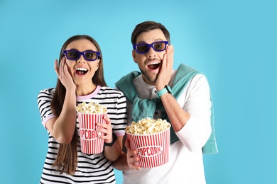 Photo of Emotional couple with 3D glasses and tasty popcorn on color background