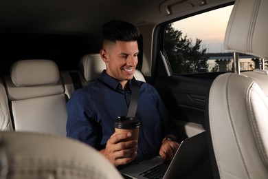 Photo of Businessman with cup of drink and laptop in modern taxi
