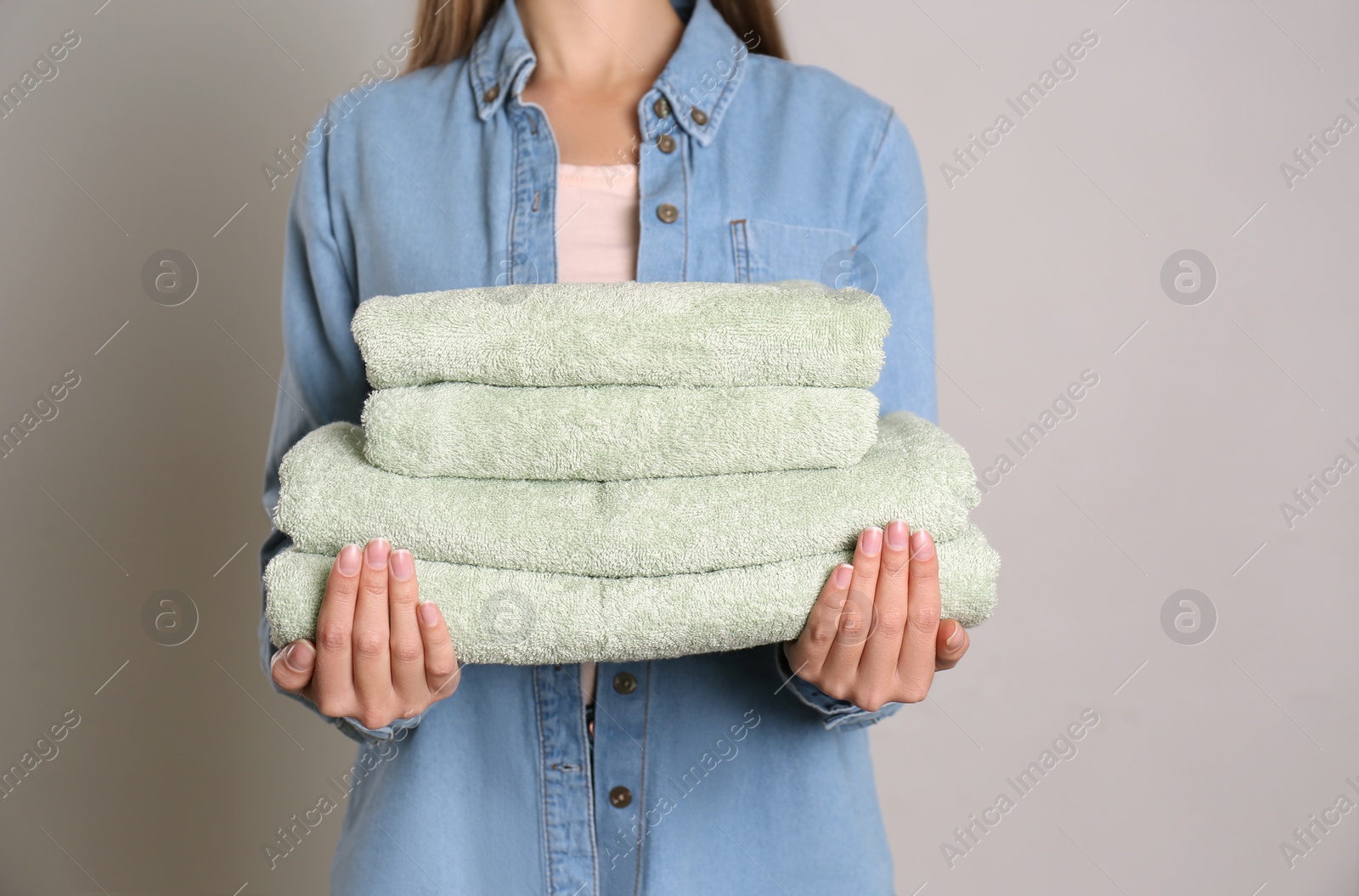 Photo of Woman holding stack of fresh towels on grey background, closeup