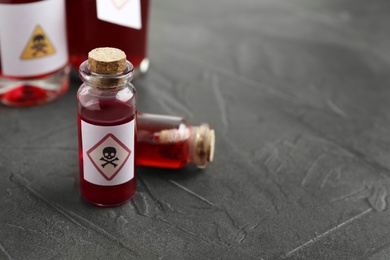 Photo of Glass vials of poison with warning sign on grey stone table, closeup. Space for text