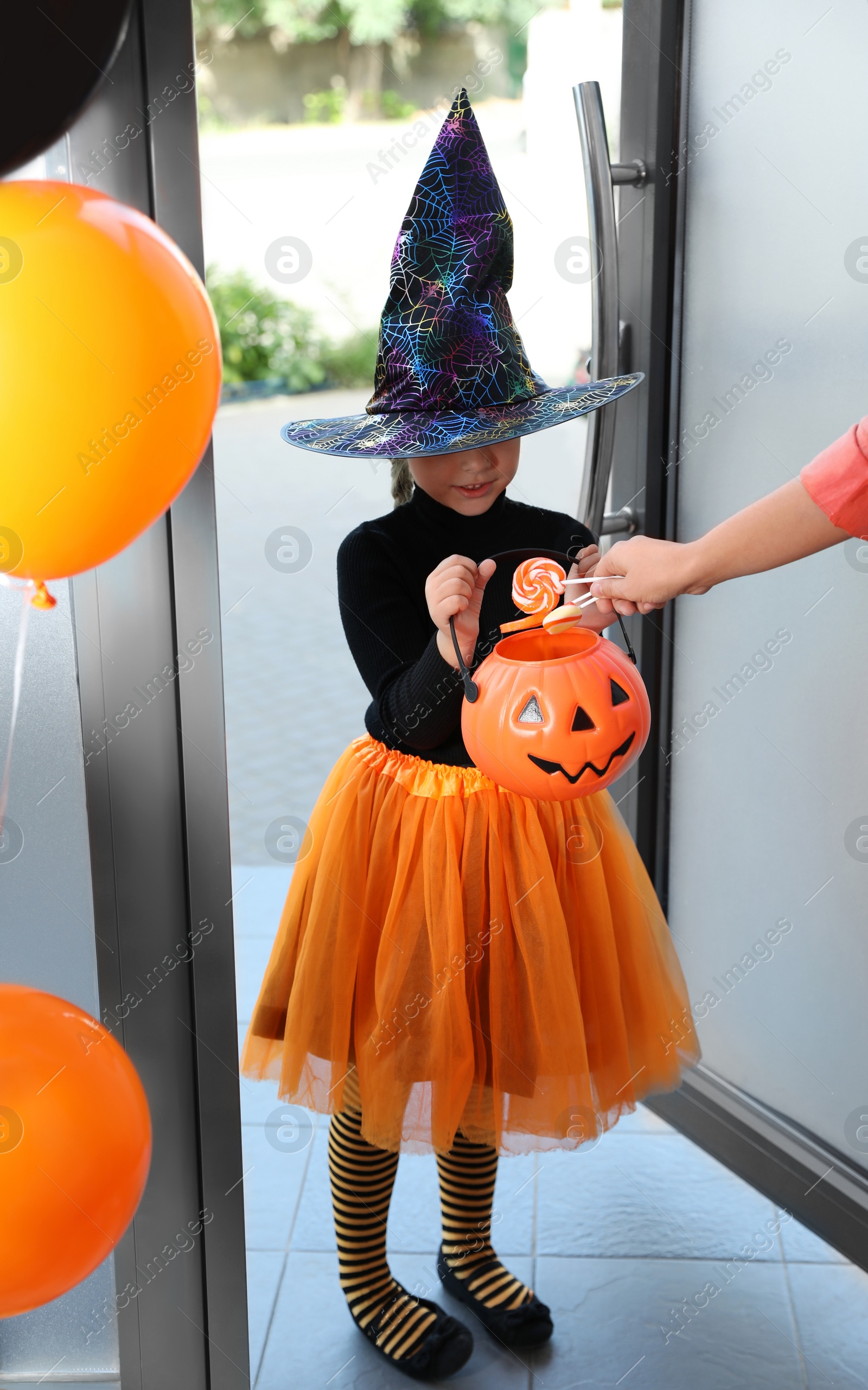 Photo of Cute little girl dressed as witch trick-or-treating at doorway. Halloween tradition