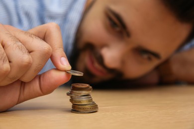 Photo of Man stacking coins at wooden table, focus on hand. Money savings