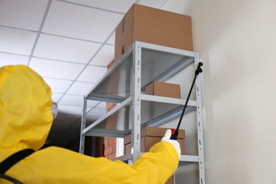 Pest control worker spraying pesticide on rack indoors