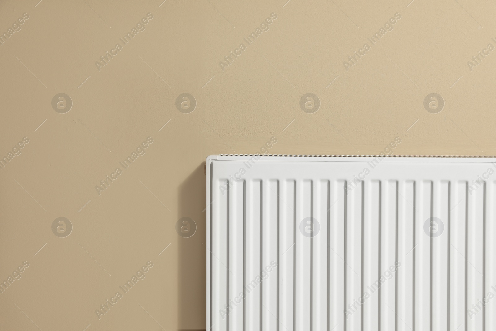 Photo of Modern radiator on beige wall, space for text. Central heating system