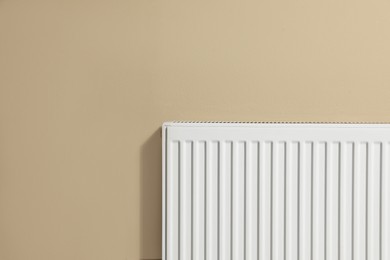 Photo of Modern radiator on beige wall, space for text. Central heating system