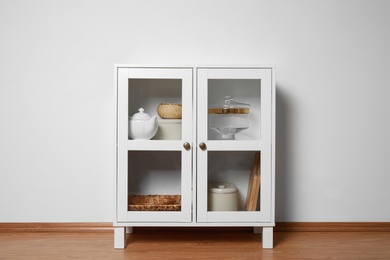 Wooden cabinet with kitchenware near white wall