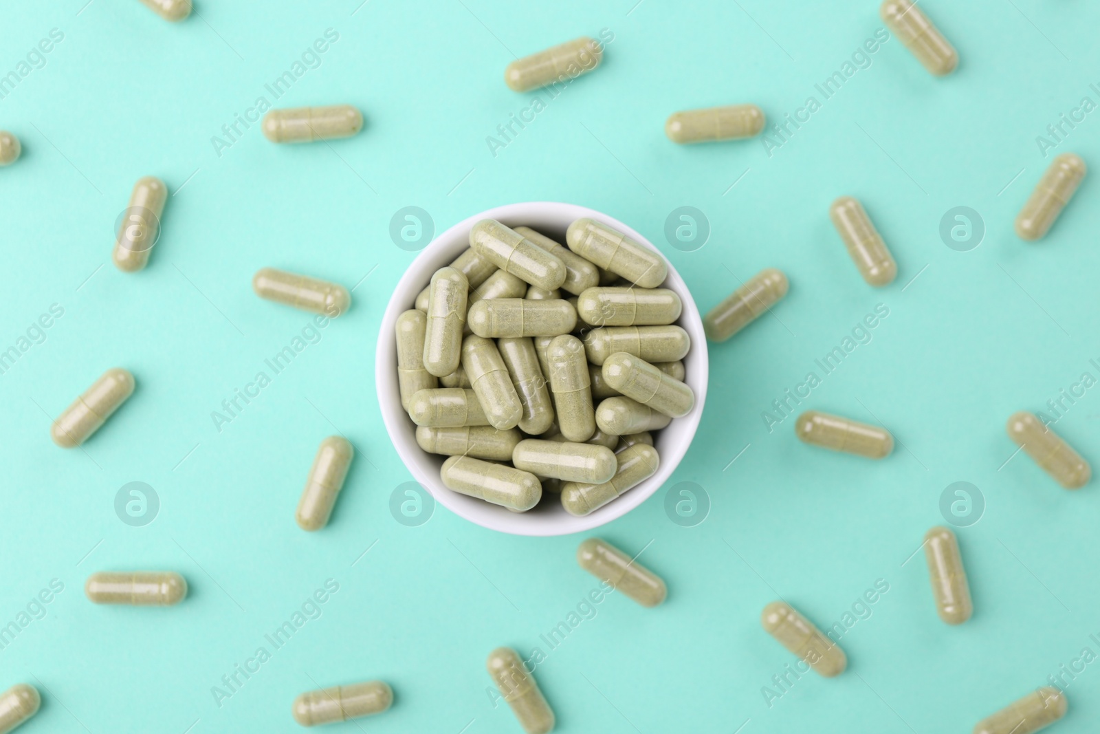 Photo of Bowl with vitamin capsules on turquoise background, flat lay