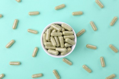 Bowl with vitamin capsules on turquoise background, flat lay