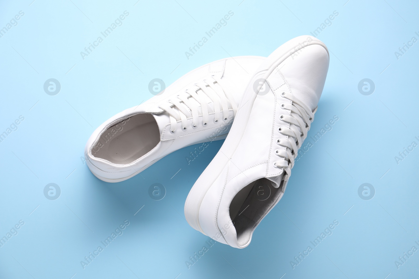 Photo of Pair of stylish white sneakers on light blue background, top view