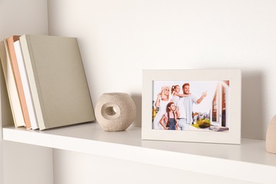 Photo of Photo frame with family portrait and books on white shelf indoors