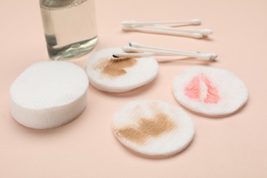 Photo of Dirty cotton pads after removing makeup, buds and bottle of cosmetic product on beige background, closeup