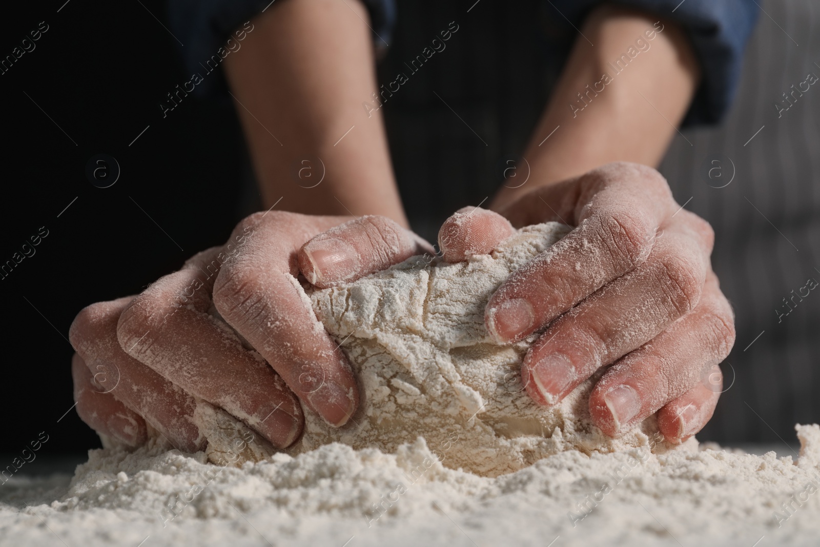 Photo of Making bread. Woman kneading dough at table on dark background, closeup