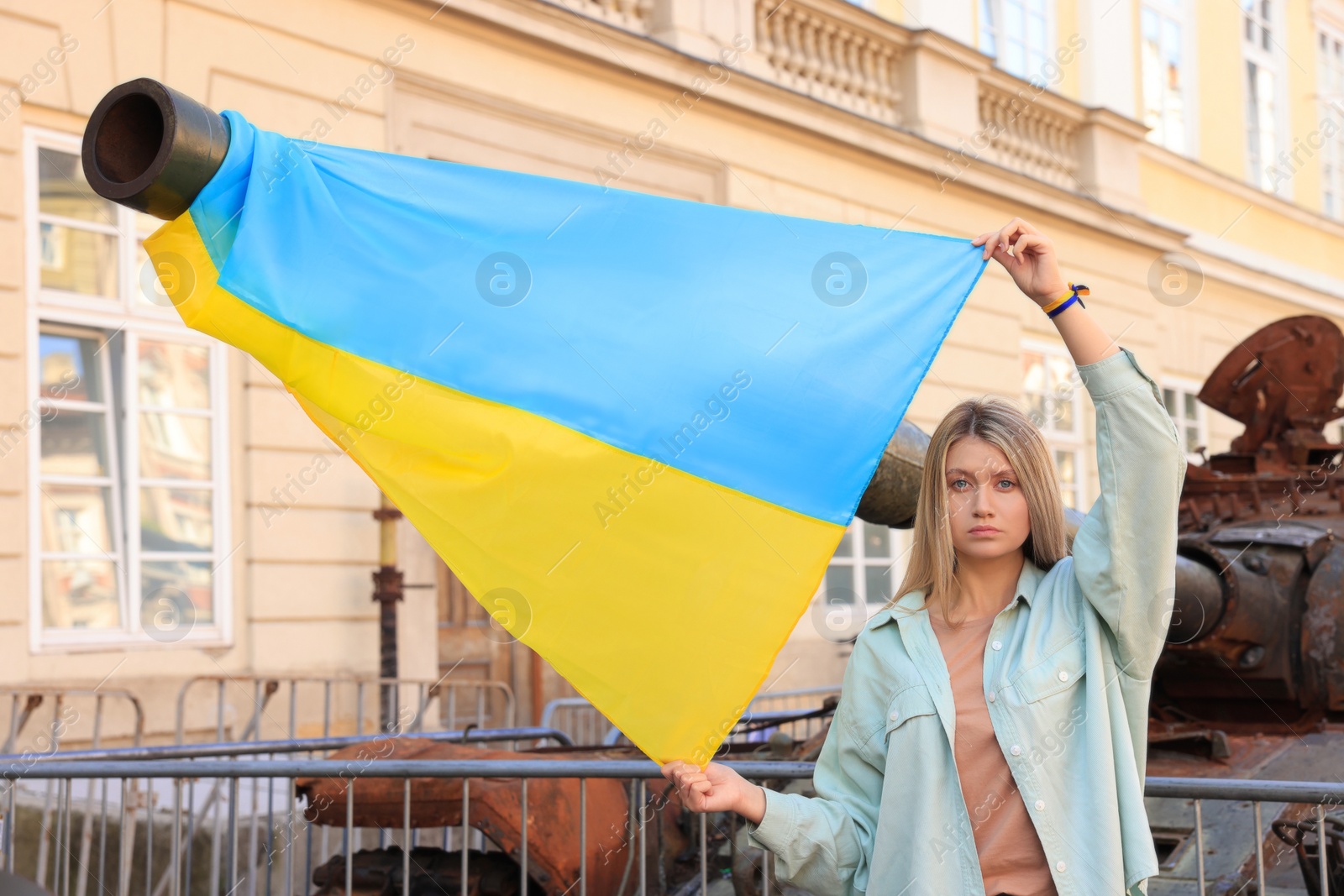 Photo of Sad woman holding Ukrainian flag near broken tank in city