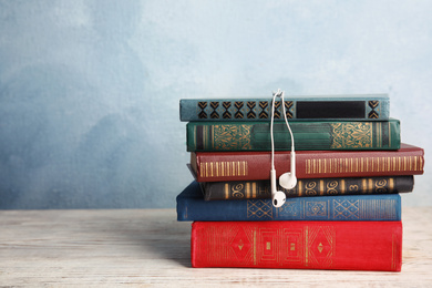 Earphones and stack of books on white wooden table. Space for text