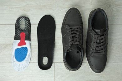 Photo of Orthopedic insoles near shoes on floor, flat lay