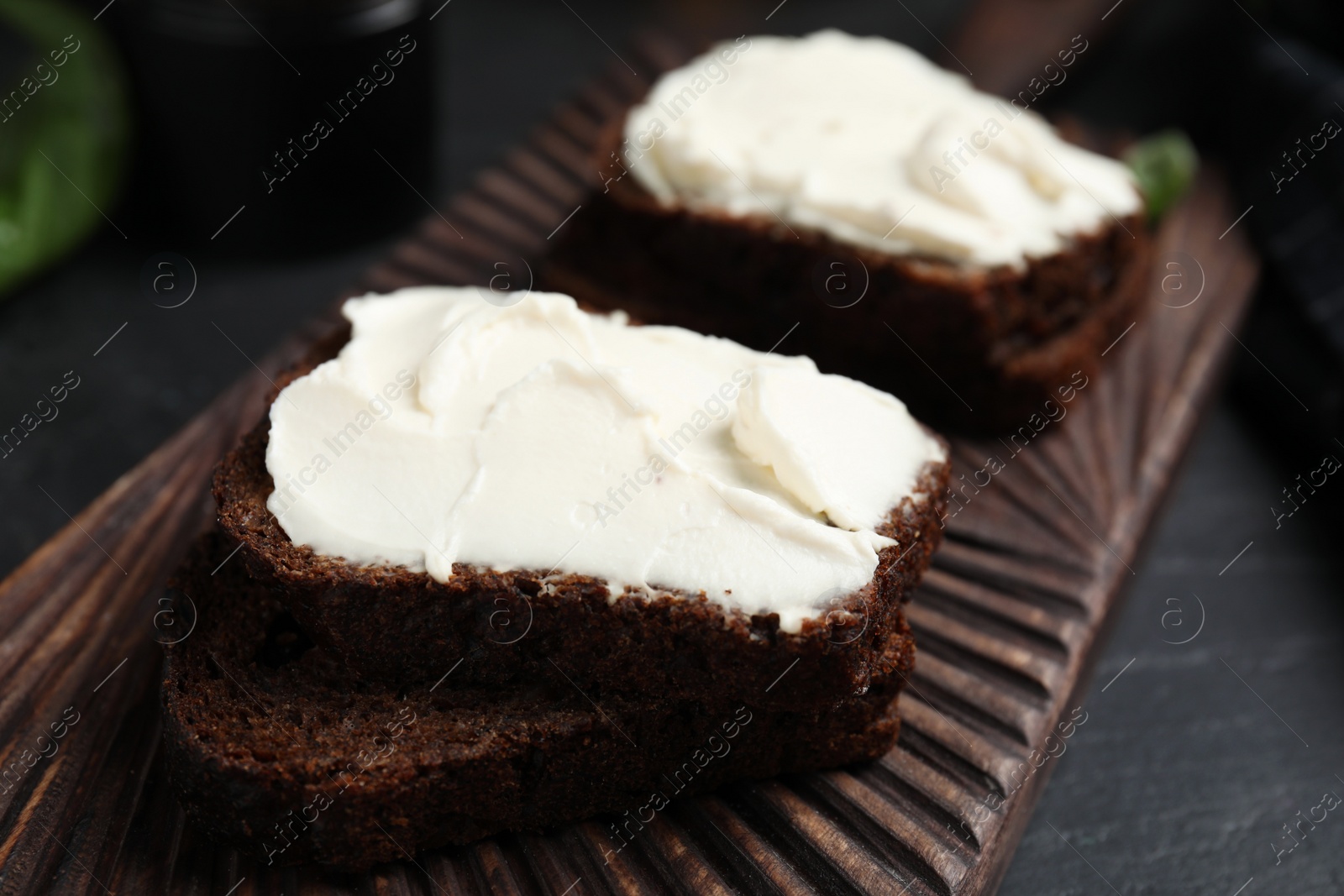 Photo of Bread with cream cheese on wooden board, closeup