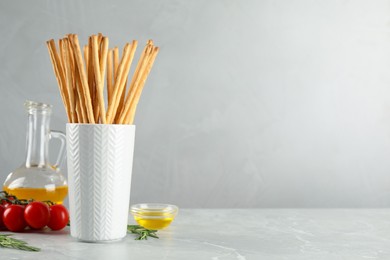 Delicious grissini sticks, oil, rosemary and tomatoes on grey marble table. Space for text