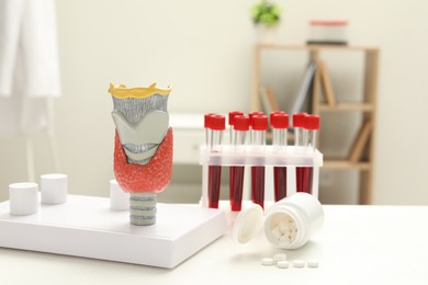 Photo of Endocrinology. Model of thyroid gland, bottle with pills and samples of blood in test tubes on white table at clinic