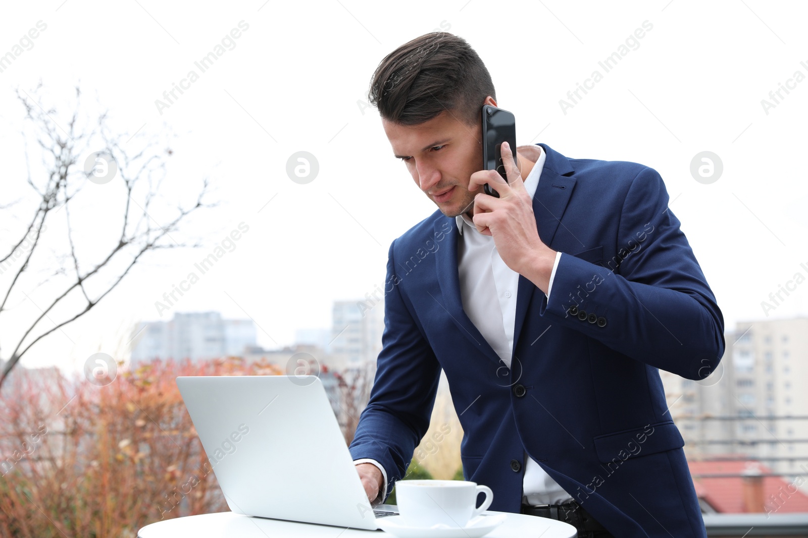 Photo of Businessman with laptop talking on phone in outdoor cafe. Corporate blog