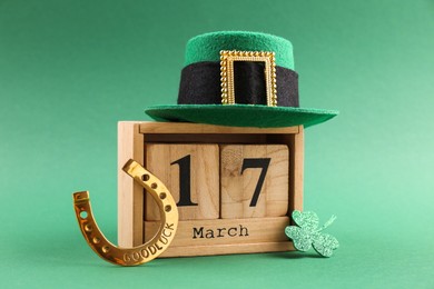 Photo of St. Patrick's day - 17th of March. Wooden block calendar, leprechaun hat, golden horseshoe and decorative clover leaf on green background