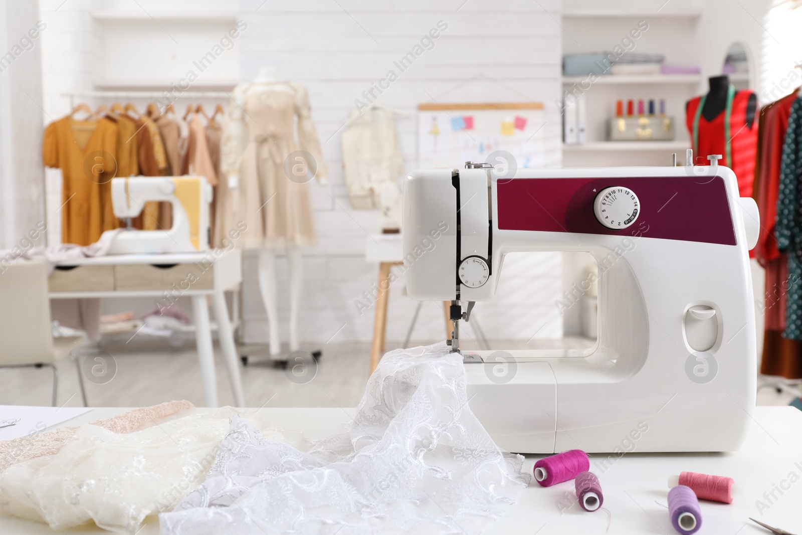 Photo of Modern sewing machine with fabric and bright threads on table in dressmaking workshop