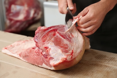 Butcher cutting fresh raw meat on counter in shop, closeup