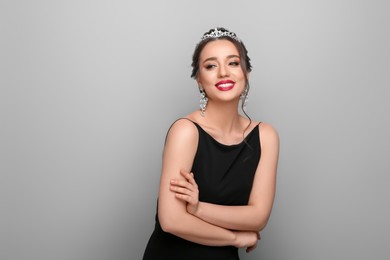 Beautiful young woman wearing luxurious tiara on light grey background, space for text