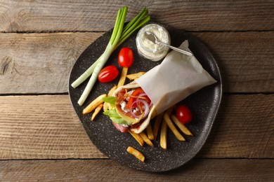 Delicious pita wrap with prosciutto, vegetables and potato fries on wooden table, top view