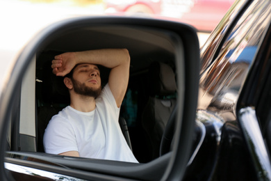 Photo of Tired man sleeping in his auto, view through car side mirror