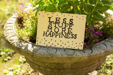Card with phrase Less Stuff More Happiness on stone planter outdoors