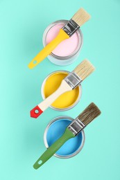 Cans of paints with brushes on turquoise background, flat lay