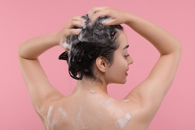 Photo of Woman washing hair on pink background, back view