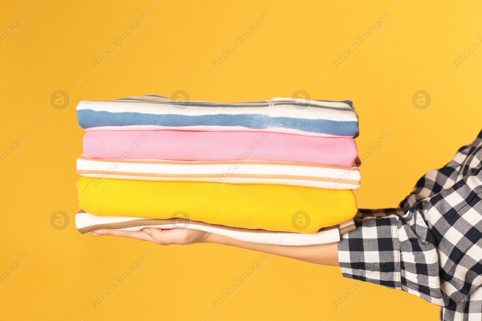 Photo of Young woman holding clean laundry on color background, closeup