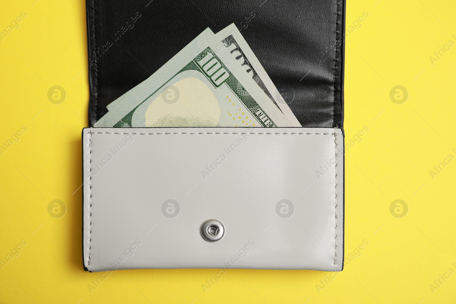 Photo of Stylish leather purse with dollar banknotes on yellow background, top view