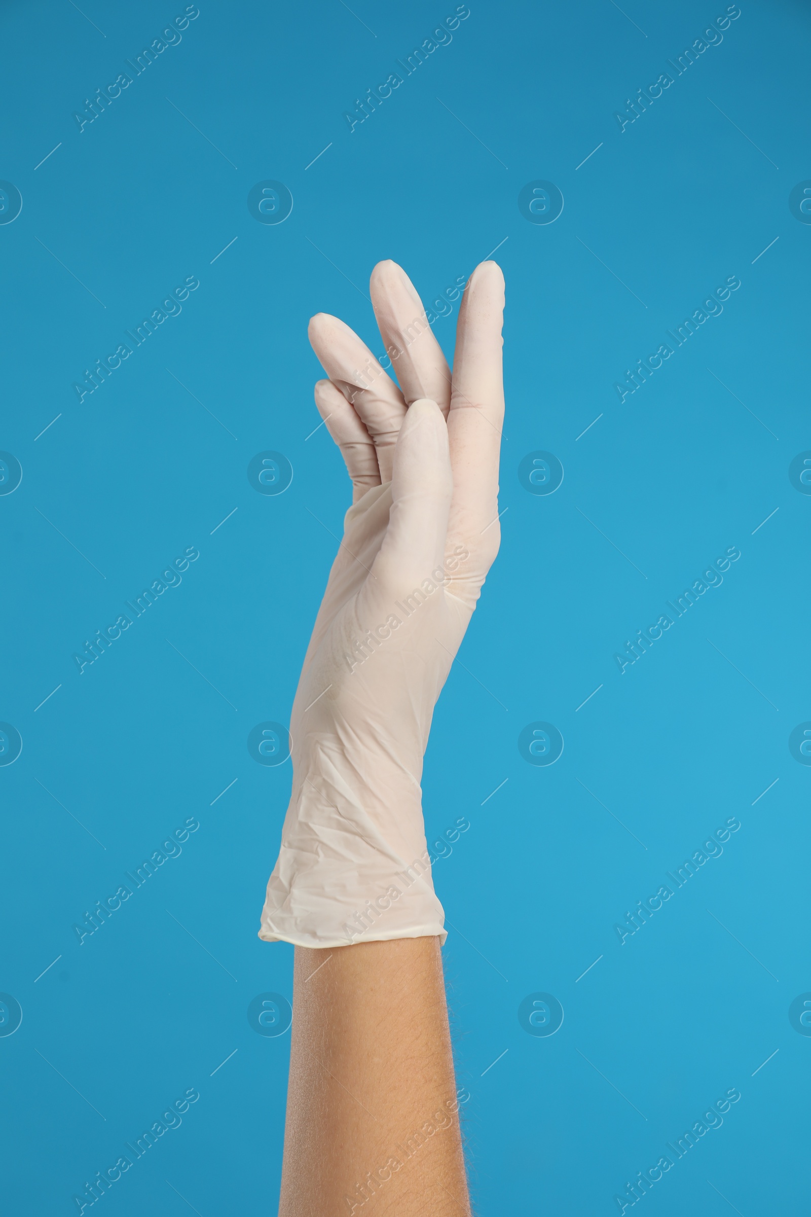 Photo of Doctor wearing medical gloves on light blue background, closeup