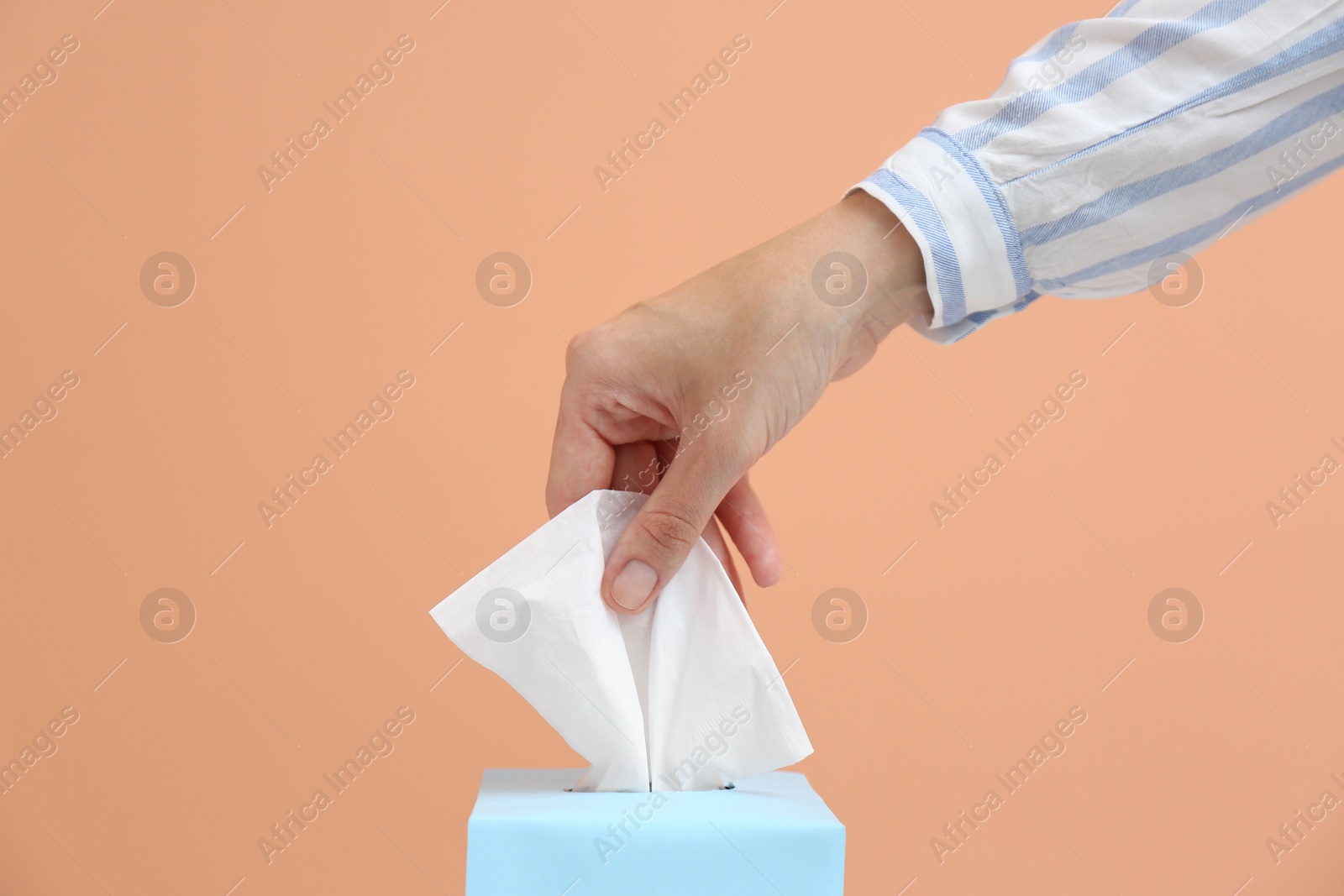 Photo of Woman taking paper tissue from box on light brown background, closeup