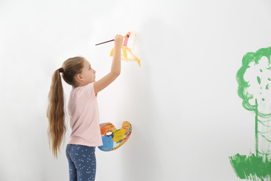 Photo of Little child painting on white wall indoors