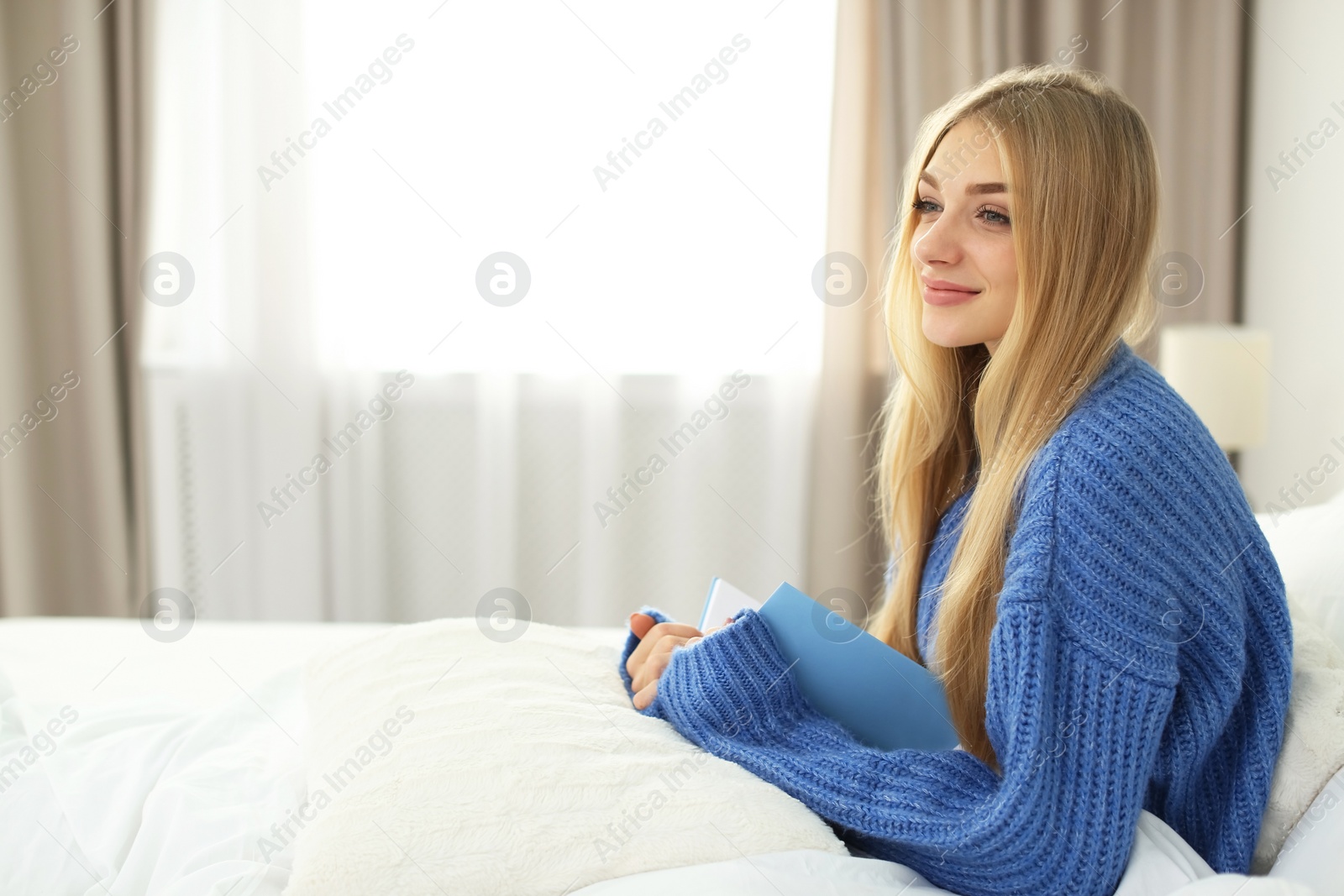 Photo of Beautiful young woman sitting with book in bed and dreaming at home. Winter atmosphere